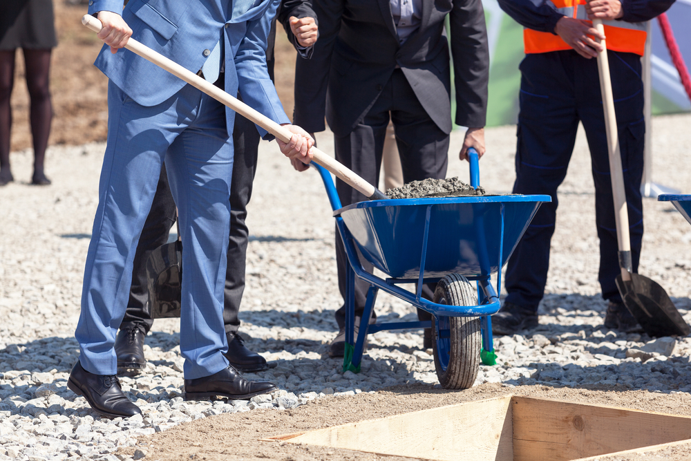 Business professionals in suits shoveling cement at construction site, showing partners doing development work instead of marketing